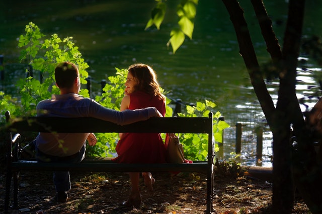 Muž a žena sedia na lavičke vedľa jazera a usmievajú sa na seba