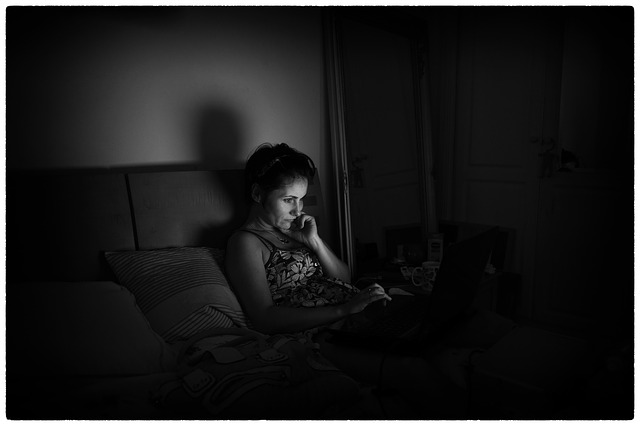 Žena sedí na posteli, pozerá do notebooku a má tvár osvietenú svetlom.jpg